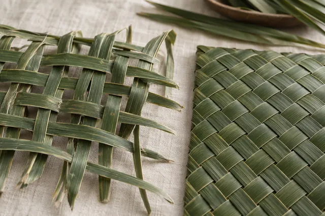 A half-finished palm leaf basket showing loose weaving beside a neatly finished one