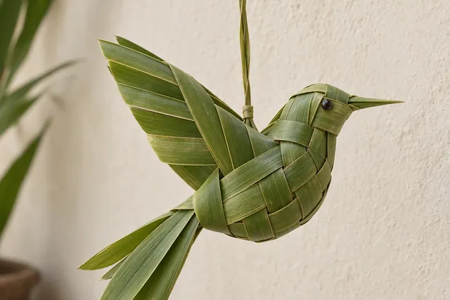A folded green coconut leaf bird resting on a pale wooden table